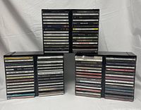 Three black plastic CD stands filled with 90 CDs in total, arranged upright showing the front of the CD spines.
