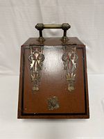 Front view of the antique coal scuttle showing wooden handle and decorative brass hinges on brown painted metal body.