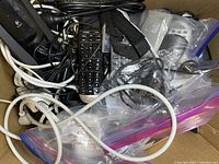 Box filled with tangled black and white wires, remote control, power adapter, and electronic accessories.
