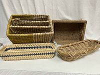 Five assorted woven baskets arranged on a white surface: large three-section basket, basket with glass handle, seagrass basket, narrow rectangular basket with blue stripe, and long bread basket.
