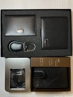 Box containing multiple black leather wallets and a black leather keychain with metallic accents all seated in black foam padding.