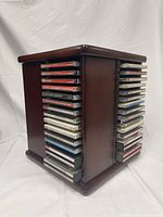 Wooden rotating CD stand holding vertical CDs, showing multiple sides of the turntable-style stand with classical CD jewel cases visible