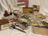 Wide view showing assorted craft supplies including fabric pieces, scissors, stapler, tape, thread, small wooden easel, and crocheted rooster figure.