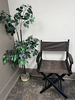 Full view of the folding directors chair with black frame and dark brown fabric, positioned near an artificial plant.