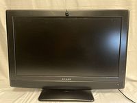 Front-facing image of a Dynex 32-inch flatscreen TV, showing the full screen and base stand.