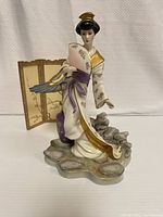 Front view of the Franklin Mint Michiko Princess of the Plum Blossoms porcelain figurine with fan, standing on a rock base with a decorative screen behind.