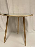 Side view of round glass topped side table showing wooden legs and under glass particle board top.