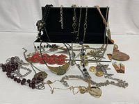 Mirrored hinged jewelry organizer box with assorted costume jewelry laid out in front and hanging inside lid.