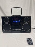 Front view of JVC sound system with speakers and remote, showing digital display lit with blue light and original iPod dock on top