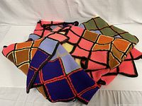 Afghan folded showing various colored square patches with black knitted border lines in pink, green, blue, orange and brown tones.