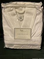Front view of Kassatex Spa Robe packaged in plastic zipper bag, showing label with size L/XL and fiber content.