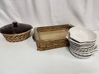 Anchor Hocking covered casserole dish in woven wicker basket with six white scalloped dishes and Pyrex rectangular glass dish with leather handles grouped together