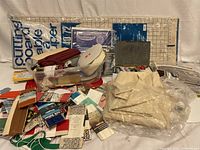 Overview of the entire sewing accessories lot including cutting board, ribbons, fabric pieces, thread spools, and containers