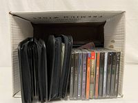 Box containing approximately 30 assorted CDs in jewel cases and two black zippered disc cases.