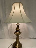 Full view of the table lamp showing beige cloth shade and brass base against white backdrop