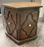 Angle view of vintage wooden side table showing carved cabinet doors with round metal knobs and base molding.