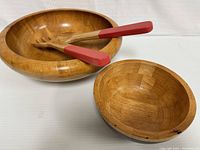 View of large and small wooden salad bowls with wooden salad serving spoons featuring red handles inside the large bowl.