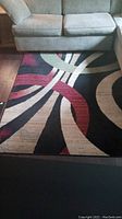 Abstract multicolor rug with curved lines in black, beige, red, and green under a beige sofa