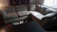 Tan chenille L-shaped sectional sofa showing three pieces arranged with lounge on the left side. Sofa sits on multicolor patterned rug in a room with window light.