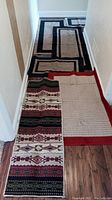 Six rugs arranged in hallway showing various colors and patterns including black, tan, red, and southwestern style patterns.