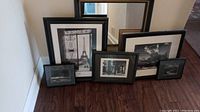 Five black and white framed art prints and one black-framed mirror arranged on floor, showing size relationship and overall lot contents.