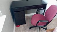Side angle showing the black desk with drawers and cabinet, and red office chair beside it.