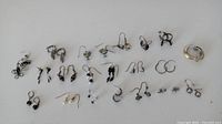 Photo showing 20 pairs of assorted small earrings in various styles including hoops, drop, and studs in silver and black tones.