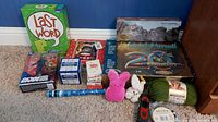 Lot of games, toys, puzzles, and craft supplies shown including board games, puzzles, stuffed animals, yarn, and boxed toys.