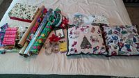 Photo showing Christmas wrapping paper rolls, gift bags, tissue paper, 4 Christmas glasses with holly decorations and gold rims, Christmas pillows, plastic ornaments, and basket with cards