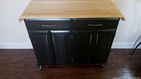 Front view of the black kitchen cart showing two drawers and two cabinet doors with silver handles and light wood top.