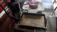 Full view of kitchen items on glass table including Waring Pro juicer, metal tray with legs, purple Corning Vision pot on a decorative white tray, and wooden tray with black printed text.