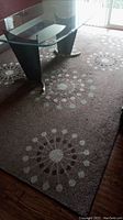 Photo of light brown rug with circular floral pattern and glass coffee table on top.