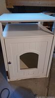 Front view of the white cat litterbox house showing the door with an arched opening and the flat top shelf with side towel rack.