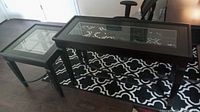 Photo showing matching black wood sofa table and square end table with glass tops and metal leg accents on a patterned rug