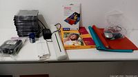 Photo showing various office supplies including photo paper packs, paper shredder, pencil sharpener, CD/DVD cases, camera case, binders, mouse, and Thunderbolt Ethernet adapter.