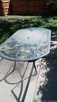 Metal framed patio table with clear glass top shown outdoors on patio.