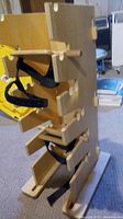 Side view of wooden multi-positioning physical therapy tower showing foot pedals with black straps and wooden peg slots.
