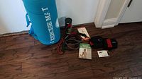 Turquoise foam exercise mat, Pilates DVD, two resistance bands, ankle weights, and shaker bottle on wood floor.