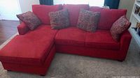 Red microfiber couch with lounge piece and four matching decorative cushions in a living room setting.