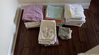 Overview of multiple stacks of towels including bath towels, hand towels, and washcloths arranged on a wooden floor.