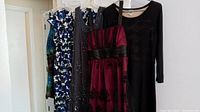 Group of five women's dresses hung on hangers, showcasing various colors and styles