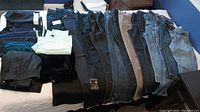 Full view of all pants laid out, showing variety of denim, black pants, and capri styles
