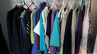 Multiple women's tops hung on hangers in a closet, showing variety in styles and colors.