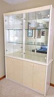 Front view of white china cabinet with glass upper doors and mirrored back, showing glass shelves with some dishware inside.