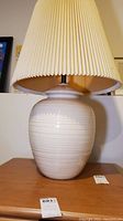 Front angle view of ceramic base table lamp with pleated cream shade showing texture and condition of shade.