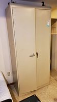 Front view of beige Sandusky metal utility cabinet with both doors closed, showing locks