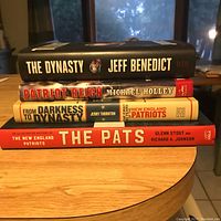Stack of four distinct hardcover sports books about the New England Patriots on a wooden surface with window background.