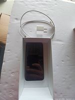 Photo shows iPhone X inside its white box with charging cable and wall adapter on white surface.
