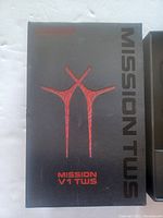 Photo of the closed black box showing the front with red stylized graphic and text 'MISSION V1 TWS' and 'Mission TWS' text on side.