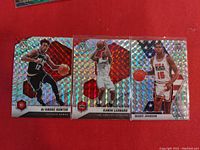 Front view of three Mosaic Prizm NBA basketball cards featuring DeAndre Hunter, Kawhi Leonard, and Magic Johnson placed on a red surface.